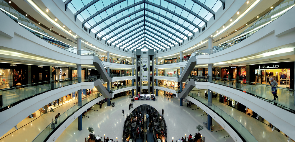 Interior de shopping con escaleras mecánicas y mensaje sobre cine, patio de comidas y promociones.